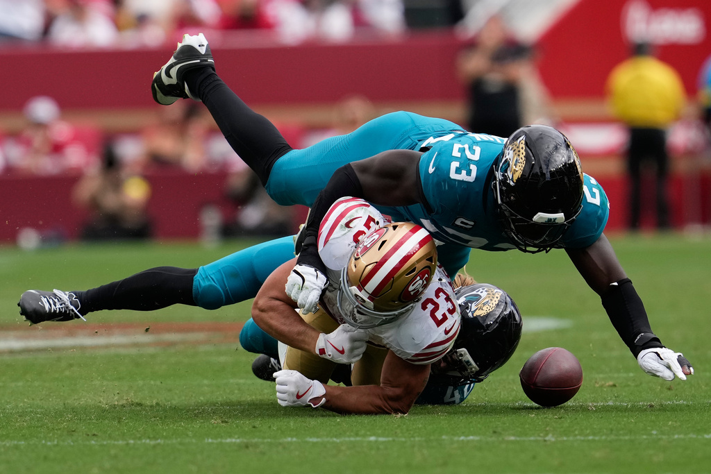 San Francisco 49ers running back Christian McCaffrey, middle, fumbles the ball, which he recovered, while being tackled by Jacksonville Jaguars linebacker Foyesade Oluokun, top, and safety Andrew Wingard during the second half of an NFL football game in Santa Clara, Calif., Sunday, Sept. 28, 2025. (AP Photo/Godofredo A. Vásquez)