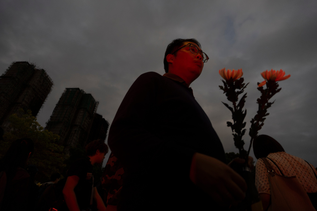 A man holding flowers arrive at the site of a deadly fire at Wang Fuk Court, a residential estate in the Tai Po district of Hong Kong's New Territories, on Tuesday, Dec. 2, 2025. (AP Photo/Ng Han Guan)