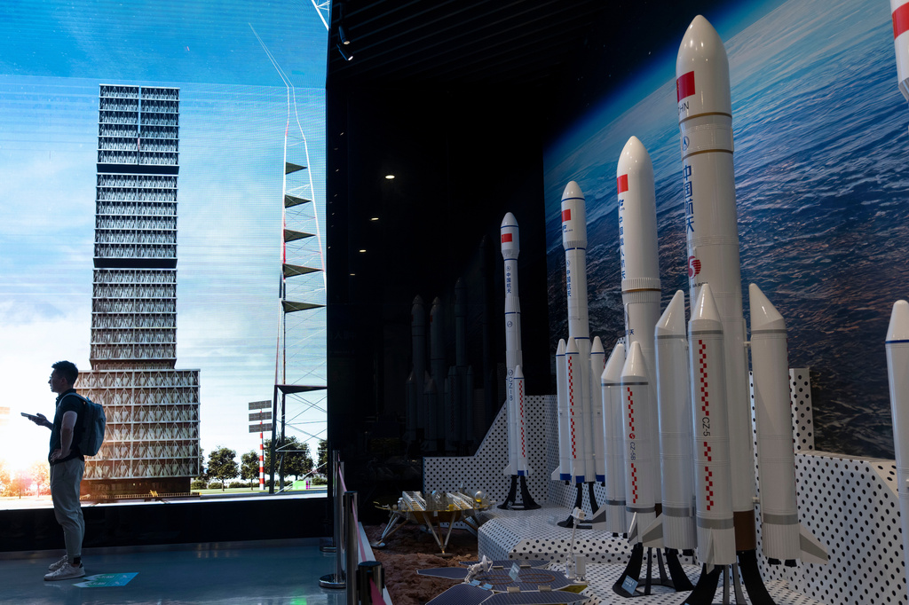 A man is silhouetted near an image of the launch platform and models of space rockets displayed in Haikou in southern China's Hainan province on Sunday, Aug. 23, 2026. (AP Photo/Ng Han Guan)