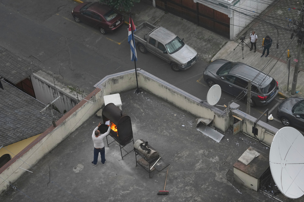 A man burns papers on a roof of the Cuban Embassy in Quito, Ecuador, Wednesday, March 4, 2026. (AP Photo/Dolores Ochoa)