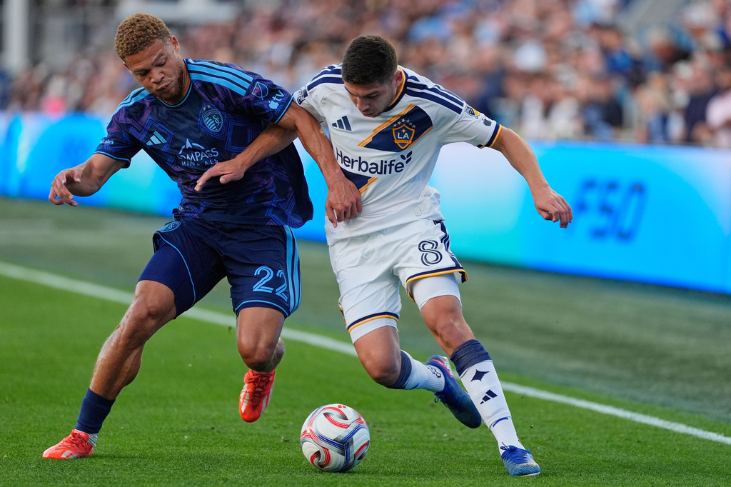 Sporting Kansas City midfielder Zorhan Bassong (22) and LA Galaxy midfielder Lucas Sanabria (8) battle for the ball during the first half of an MLS soccer match Wednesday, May 13, 2026, in Kansas City, Kan. (AP Photo/Charlie Riedel)