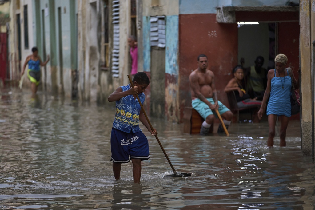 A youth sweeps away trash blocking drains on a flooded street after heavy rains in Havana, Monday, Aug. 11, 2025. (AP Photo/Ramon Espinosa)