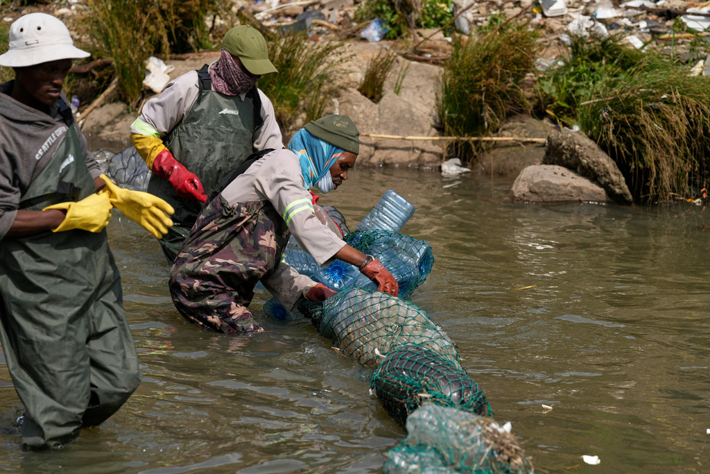 Volunteers wearing wetsuits untangle a long garbage net on the Jukskei River in the Alexandra township in Johannesburg, South Africa, Wednesday, Nov. 12, 2025. (AP Photo/Themba Hadebe)