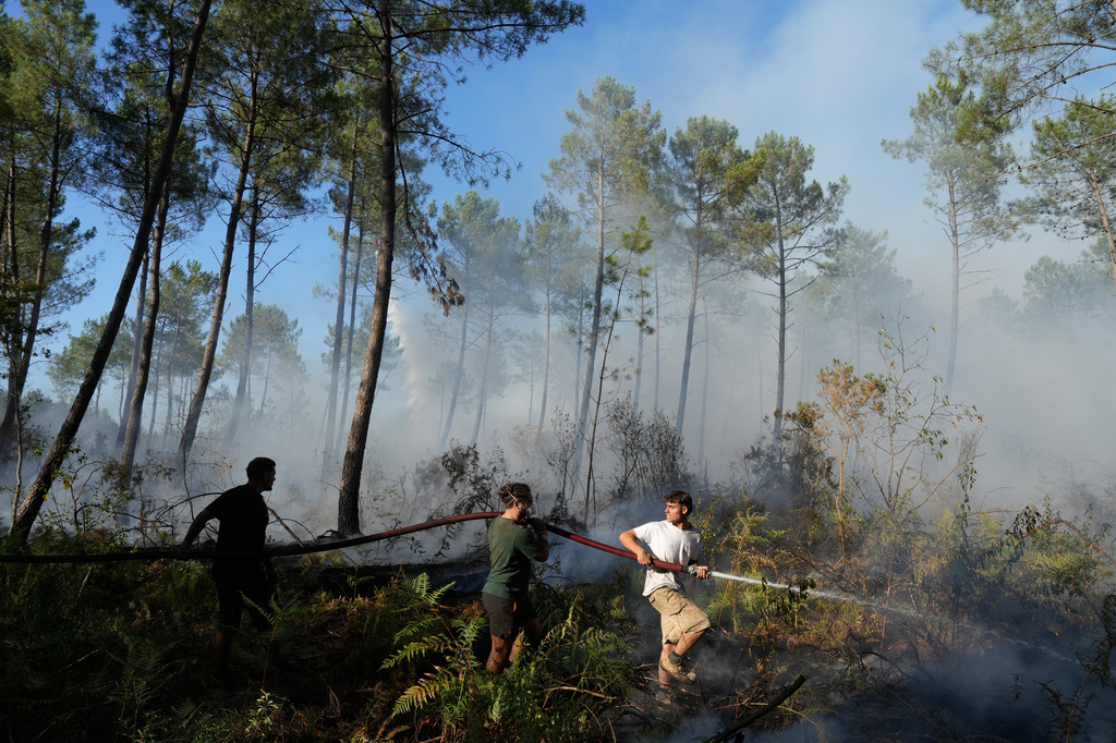 A group hold a firehose and try to suppress a fire near Lacanau, as wildfires rage outside Bordeaux, France, Monday, July 27, 2026. (AP Photo/Baz Ratner)