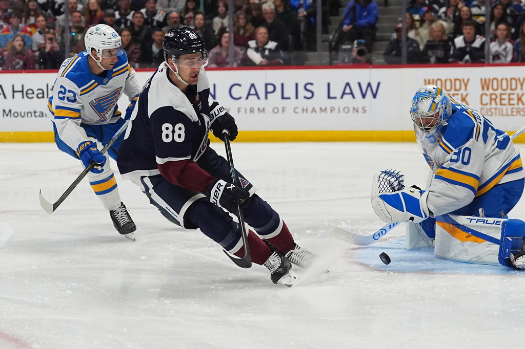 Colorado Avalanche center Martin Necas has his shot blocked by St. Louis Blues goaltender Joel Hofer, right, after drivng past defenseman Logan Mailloux in the first period of an NHL hockey game Sunday, April 5, 2026, in Denver. (AP Photo/David Zalubowski)