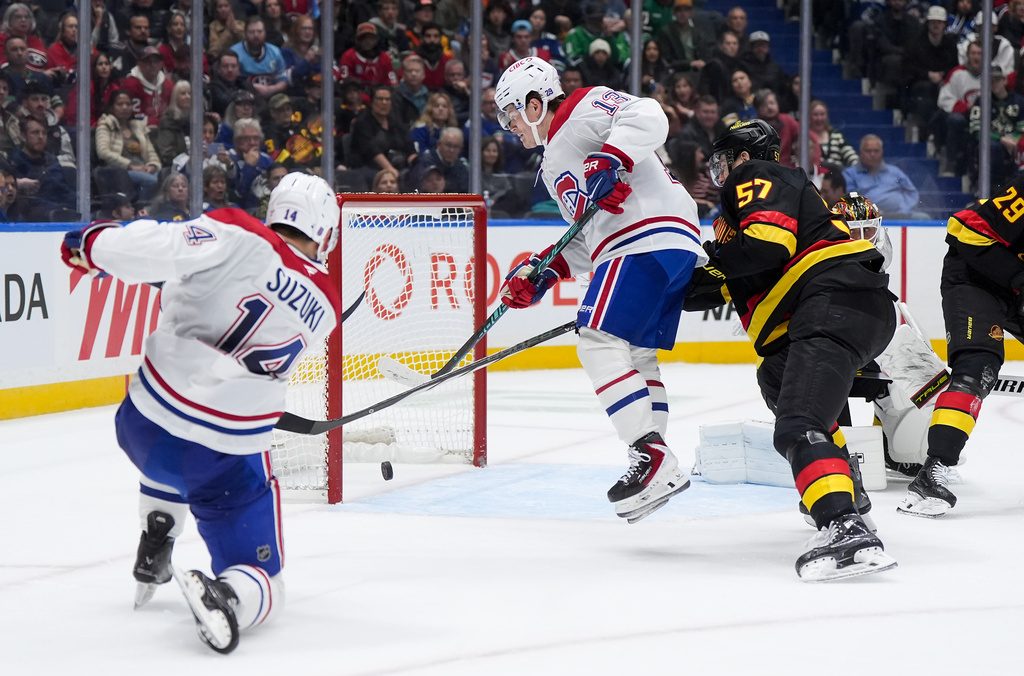 Montreal Canadiens' Nick Suzuki (14) scores into the open net behind Vancouver Canucks goalie Kevin Lankinen, back right, as Montreal's Cole Caufield (13) jumps in front of Vancouver's Tyler Myers (57) during the second period of an NHL hockey game in Vancouver, on Saturday, Oct. 25, 2025. (Darryl Dyck/The Canadian Press via AP)
