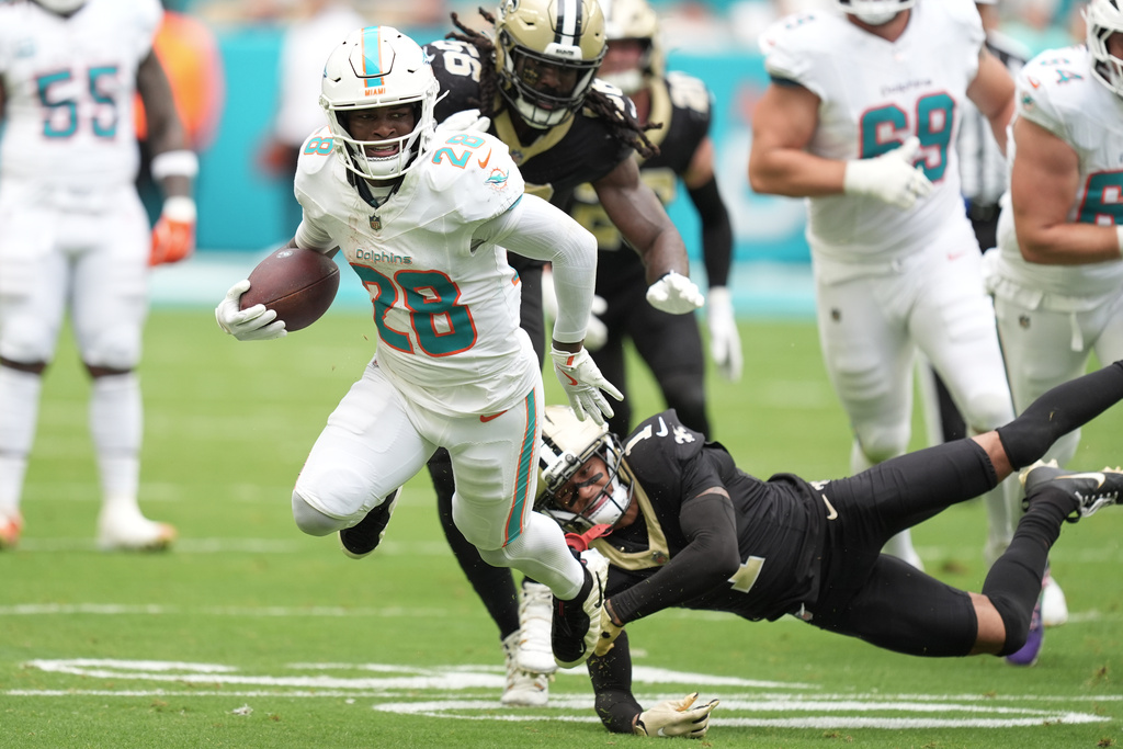 Miami Dolphins running back De'Von Achane (28) escapes a tackle by New Orleans Saints cornerback Alontae Taylor (1) during the first half of an NFL football game Sunday, Nov. 30, 2025, in Miami Gardens, Fla. (AP Photo/Rebecca Blackwell)