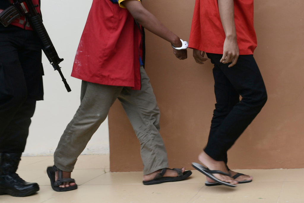A police officer escorts two men accused of having gay sex, upon arrival for their sentencing hearing at the Sharia Court in Banda Aceh, Indonesia, Monday, Aug. 11, 2025. (AP Photo/Reza Saifullah)