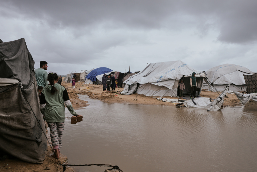 Palestinians walk through a flooded area in a temporary tent camp after heavy rainfall in Gaza City, Thursday, March 26, 2026 (AP Photo/Jehad Alshrafi)