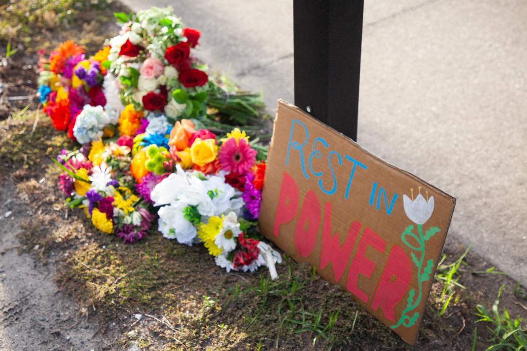 A sign reading "rest in power" is displayed alongside flowers at a vigil for a Mexican man who was struck and killed by a tractor trailer while running from an encounter with Immigration and Customs Enforcements officers the day before, Wednesday, July 15, 2026, in St. Augustine, Fla. (AP Photo/Kelly Jordan)
