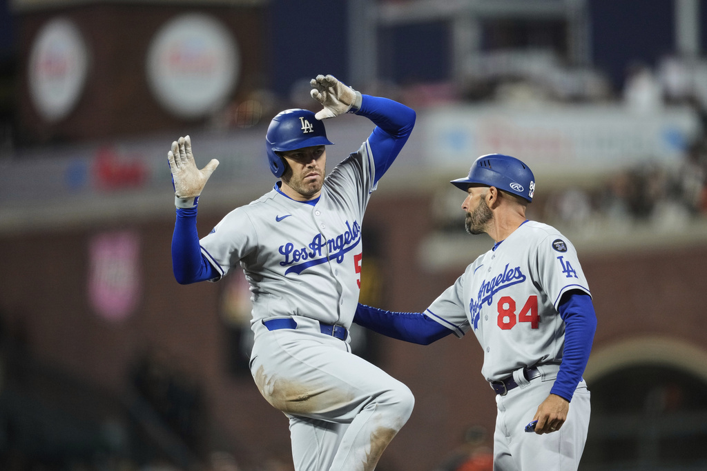 Los Angeles Dodgers' Freddie Freeman, left, celebrates with first base coach Chris Woodward after hitting a single during the fifth inning of a baseball game against the San Francisco Giants, Saturday, Sept. 13, 2025, in San Francisco. (AP Photo/Godofredo A. Vásquez)