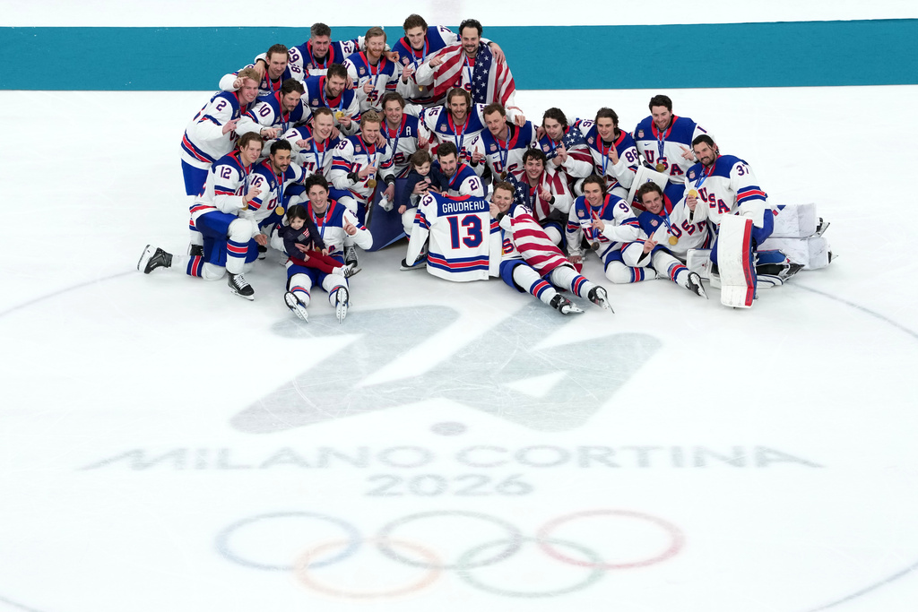 ADDS ID FOR CHILDREN United States players pose for pictures with the jersey of the late Johnny Gaudreau (13) with his daughter Noa and son Johnny after their win over Canada in the men's ice hockey gold medal game at the 2026 Winter Olympics in Milan, Italy, Sunday, Feb. 22, 2026. (AP Photo/Carolyn Kaster)