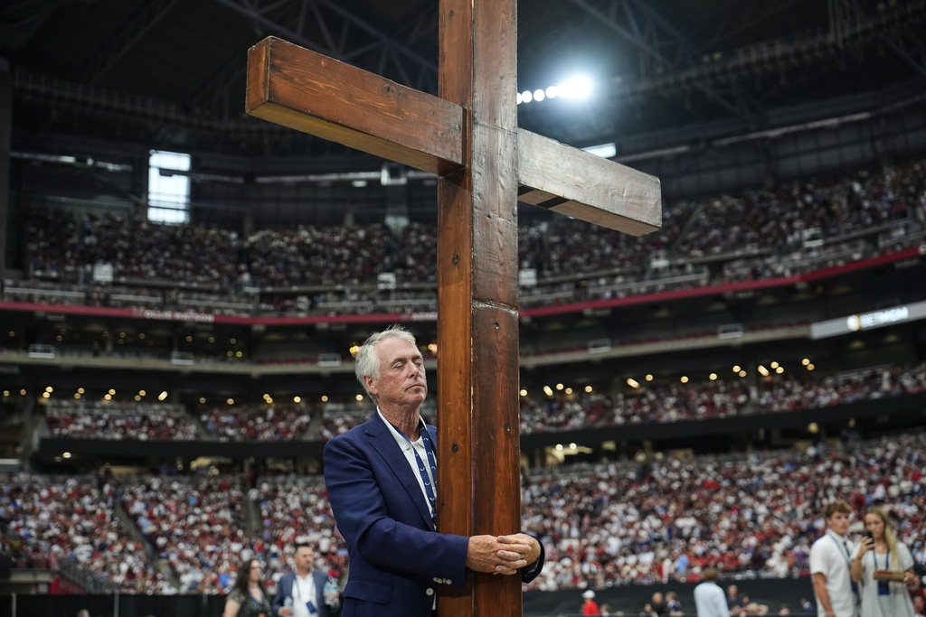 Dan Beazley stands with a cross at a memorial for conservative activist Charlie Kirk, Sunday, Sept. 21, 2025, at State Farm Stadium in Glendale, Ariz. (AP Photo/John Locher)