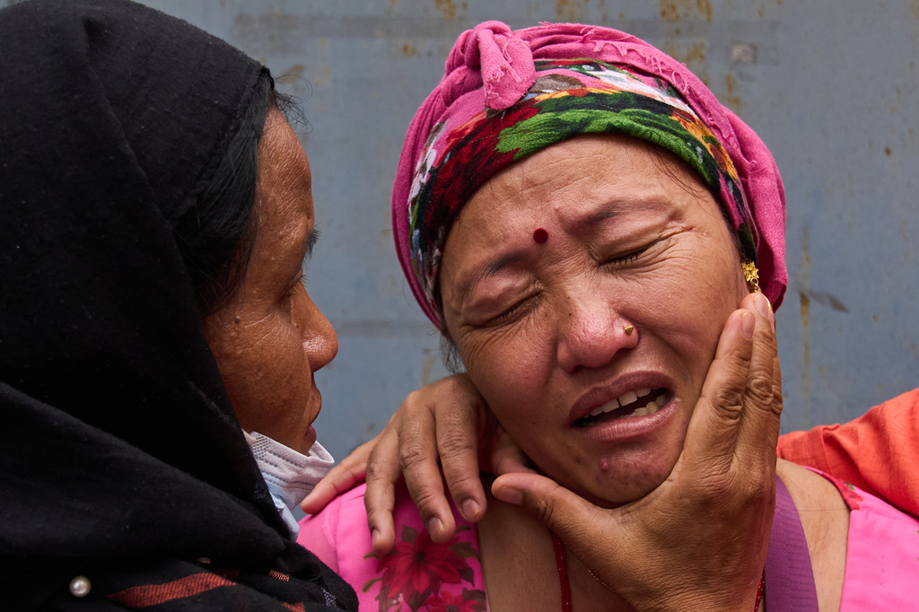Relatives comfort Jantari Gurung, whose husband is missing, as she looks at photographs of people killed in flash floods displayed outside a government hospital in Kathmandu, Nepal, Sunday, Aug. 30, 2026. (AP Photo/Dar Yasin)