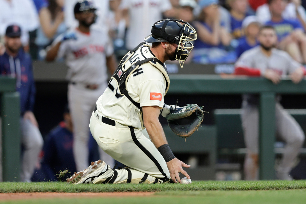 Seattle Mariners catcher Cal Raleigh picks up the ball after a scoring play by the Boston Red Sox during the seventh inning of a baseball game, Friday, June 19, 2026, in Seattle. (AP Photo/John Froschauer)