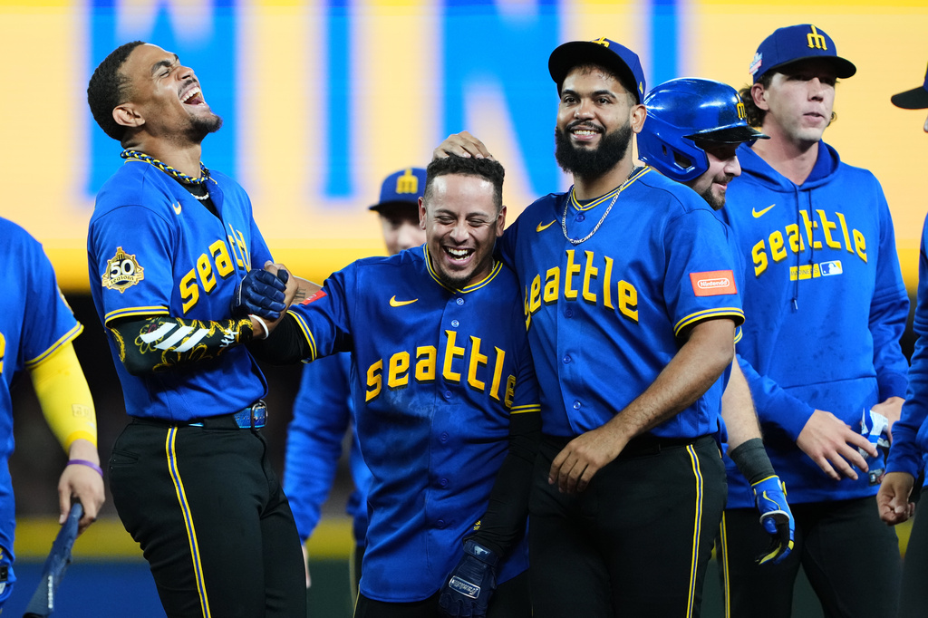 Seattle Mariners' Leo Rivas, center, celebrates with teammates Julio Rodríguez, left, and Seranthony Domínguez, third from left, after his walk-off RBI single in the 10th inning to win a baseball game against the Chicago Cubs, Friday, Aug. 21, 2026, in Seattle. (AP Photo/Lindsey Wasson)