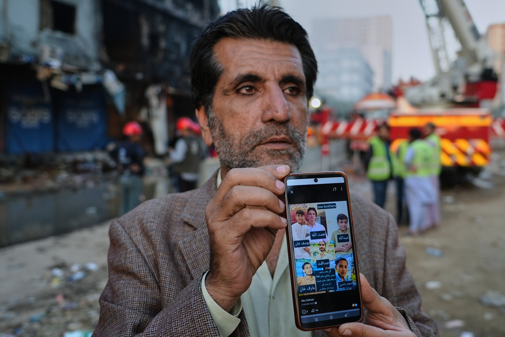 Mahmood Khan shows the press pictures of six family members who he says went missing after the fire at a multi-story shopping plaza, as he waits for information about them at the site of the fire in Karachi, Pakistan, Tuesday, Jan. 20, 2026. (AP Photo/Mohammad Farooq)