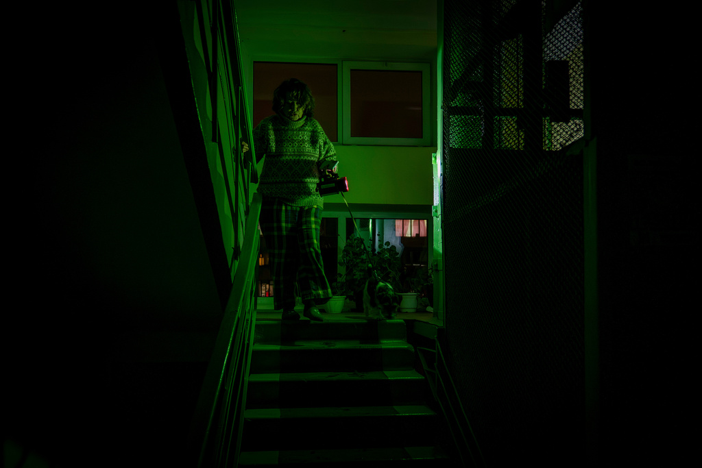Tetiana Tatarenkova shines a flashlight as she goes to see her neighbour during a blackout caused by Russia's regular air attacks against the country's energy infrastructure in Kyiv, Ukraine, Tuesday, Jan. 13, 2026. (AP Photo/Dan Bashakov)