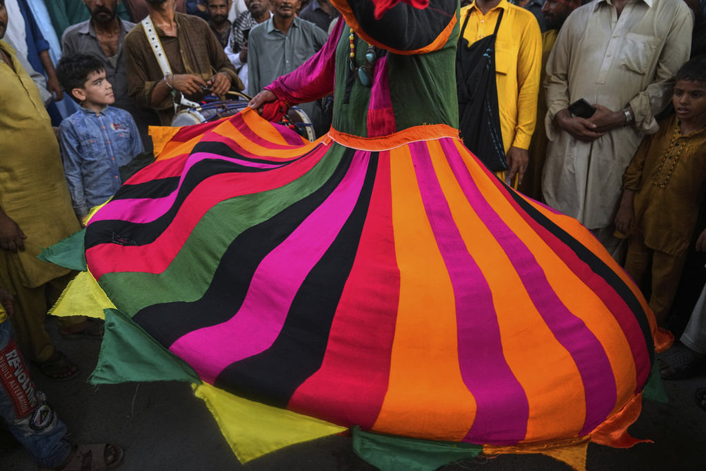 Youngsters with others look to a spiritual path devotee locally called 'Malang' performing a devotional dance called 'Dhamaal' during the celebrations of the three-day annual festival or 'Urs' of mystic and scholar Hazrat Ali Hajveri, popularly known as Data Ganj Bakhsh at his shrine, in Lahore, Pakistan, Wednesday, Aug. 13, 2025. (AP Photo/K.M. Chaudary)