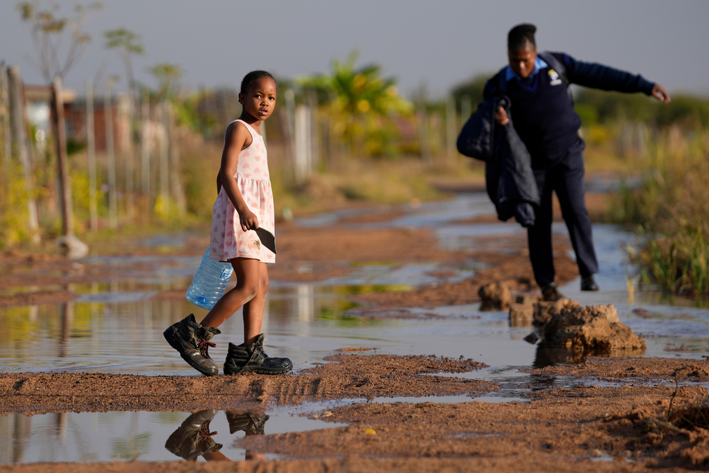 FILE — A young girl carrying an empty water bottle through a flooded street caused by an overflowing water reservoir in Hammanskraal, Pretoria, South Africa, May 26, 2023 during a cholera outbreak. (AP Photo/Themba Hadebe,File)