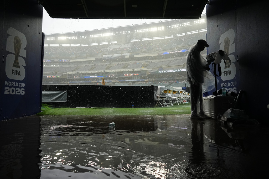 A photographer shelters from the rain as play is suspended during the World Cup Group I soccer match between France and Iraq in Philadelphia, Monday, June 22, 2026. (AP Photo/Petr David Josek)