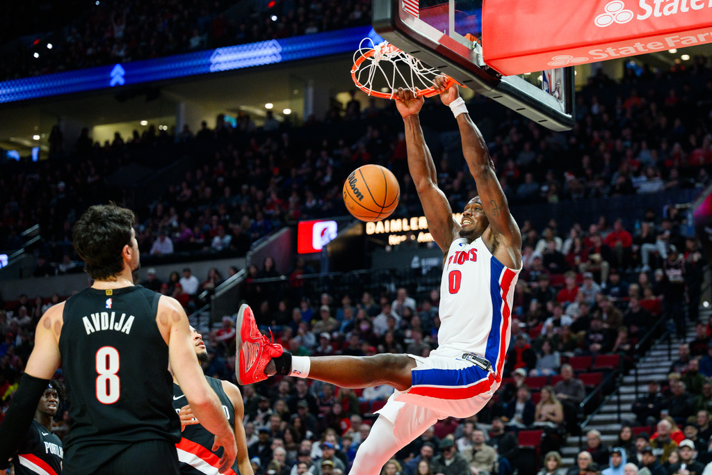 Portland Trail Blazers forward Deni Avdija (8) looks on as Detroit Pistons center Jalen Duren (0) hangs off the rim after scoring a basket during the first half of an NBA basketball game, Monday, Dec. 22, 2025, in Portland, Ore. (AP Photo/Molly J. Smith)