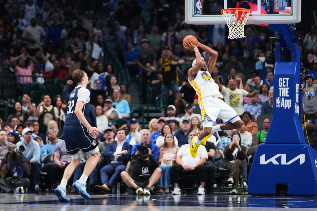 Golden State Warriors guard Moses Moody, right, reacts while suffering an injury as Dallas Mavericks forward Cooper Flagg (32) looks on during overtime of an NBA basketball game Monday, March 23, 2026, in Dallas. (AP Photo/Julio Cortez)