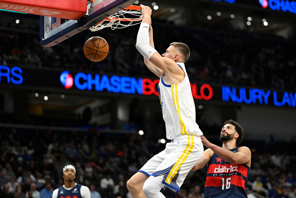 Golden State Warriors center Kristaps Porzingis, top, dunks against Washington Wizards forward Anthony Gill, right, during the first half of an NBA basketball game, Monday, March 16, 2026, in Washington. (AP Photo/John McDonnell)