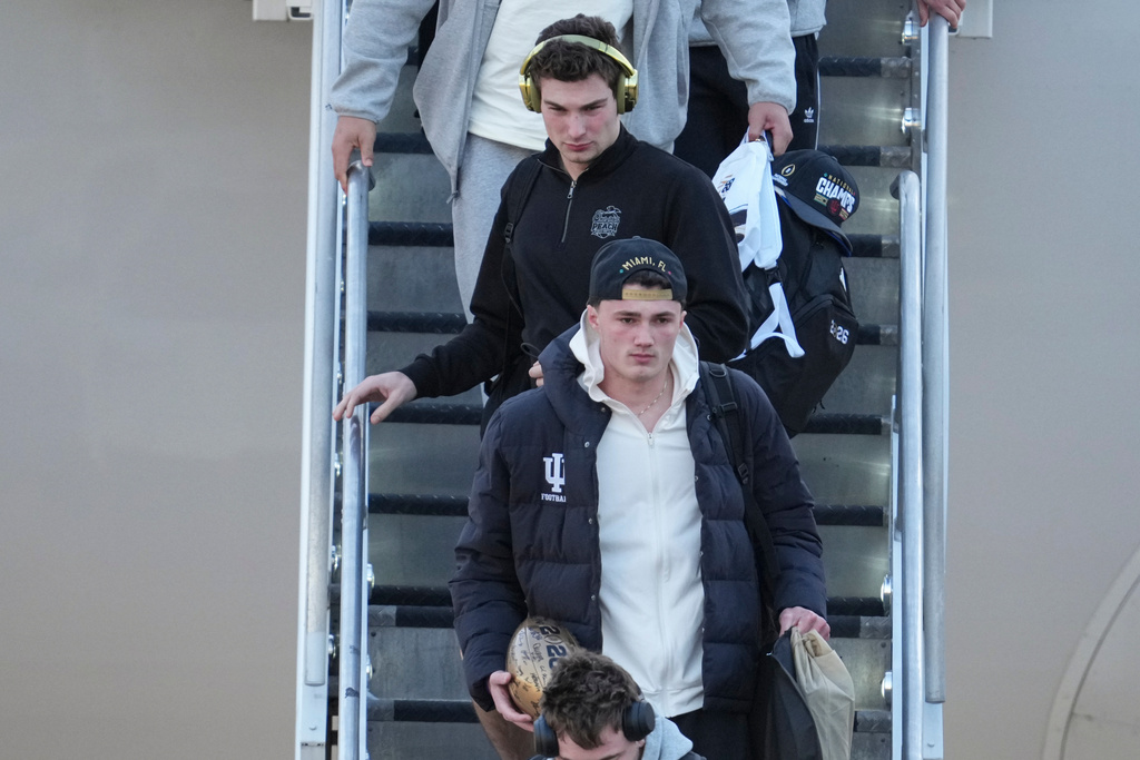 Indiana quarterback Fernando Mendoza, top, walks off the plane with teammates after they arrived at the Indianapolis International Airport in Indianapolis, Tuesday, Jan. 20, 2026. (AP Photo/Michael Conroy)