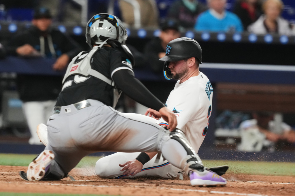 Miami Marlins Liam Hicks beats the tag by Chicago White Sox catcher Edgar Cuero (26) to score in the eighth inning during a baseball game Tuesday, March 31, 2026, in Miami. (AP Photo/Marta Lavandier)
