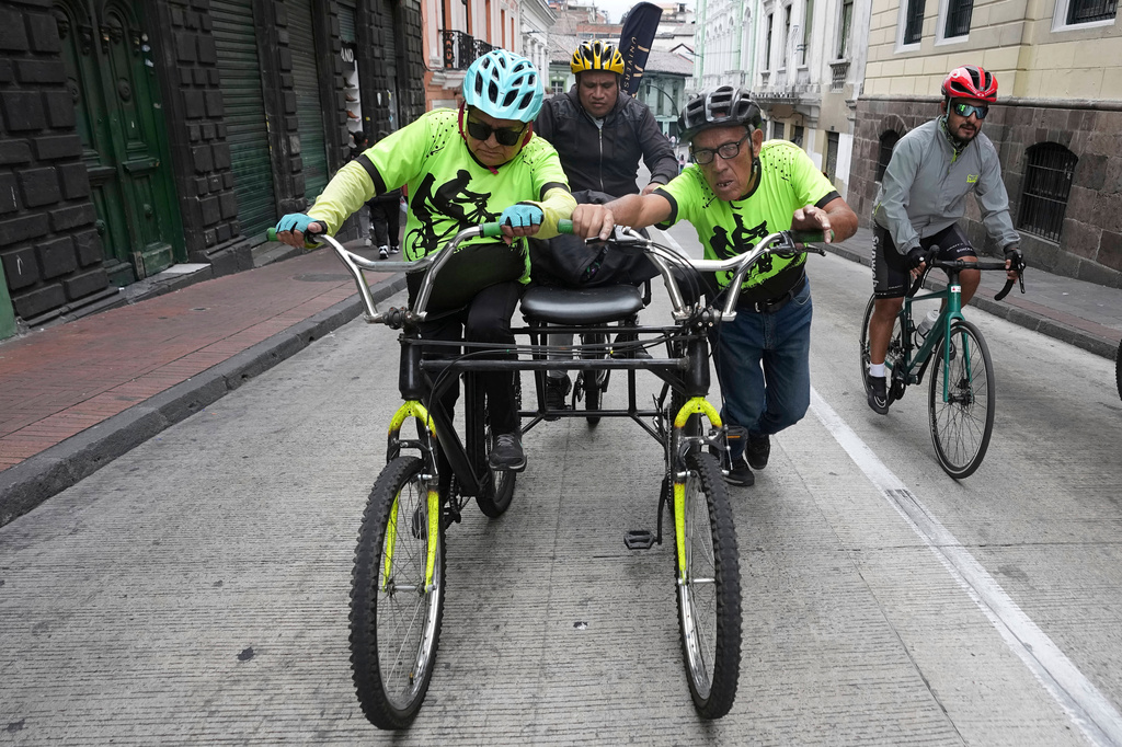 A volunteer with the "Ciegocleta" initiative, right, pushes a tandem bike for two visually impaired participants bicycle in Quito, Ecuador, Sunday, Aug. 30, 2026. (AP Photo/Dolores Ochoa)
