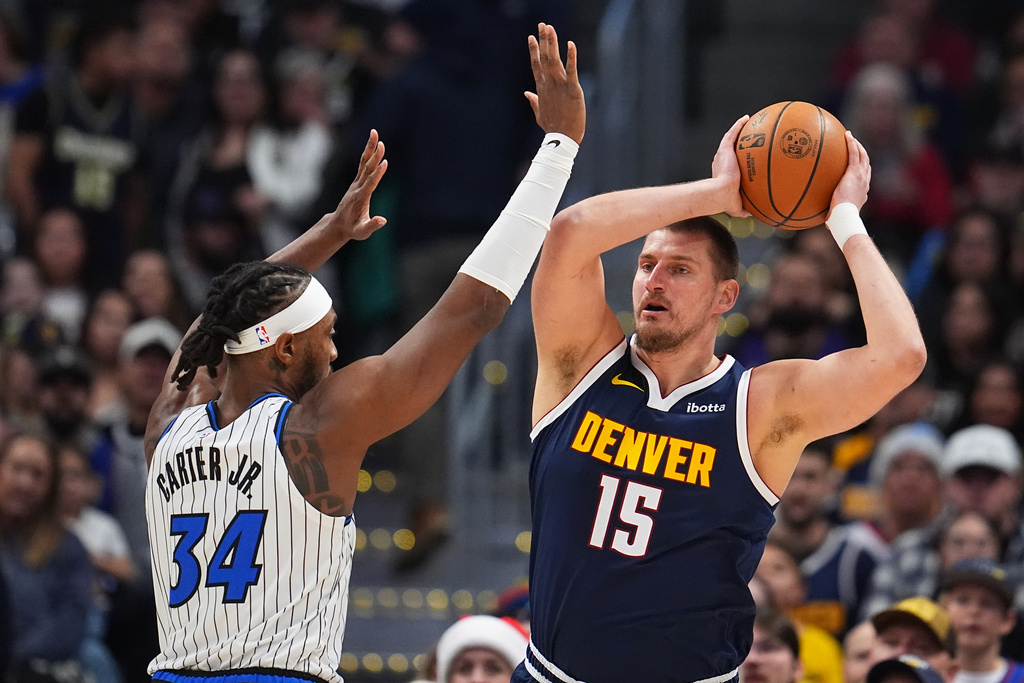 Denver Nuggets center Nikola Jokić, right, looks to pass the ball under pressure from Orlando Magic center Wendell Carter Jr. in the first half of an NBA basketball game, Thursday, Dec. 18, 2025, in Denver. (AP Photo/David Zalubowski)