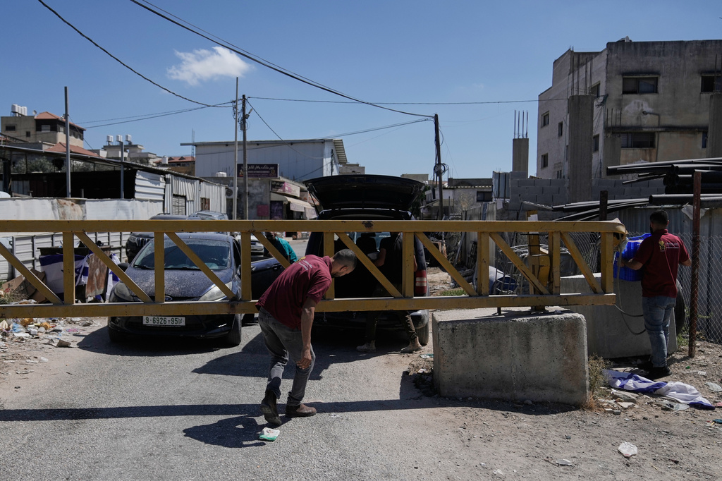 Palestinian men cross a closed gate after the Israeli army imposed a closure of the entrance to the West Bank village of Haris, Monday, Sept. 21, 2026. (AP Photo/Majdi Mohammed)