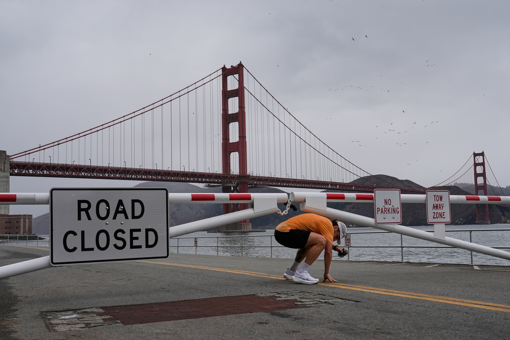 A runner ducks under a gate closing vehicle access to Fort Point National Historic Site, Wednesday, Oct. 1, 2025, in San Francisco. (AP Photo/Godofredo A. Vásquez)