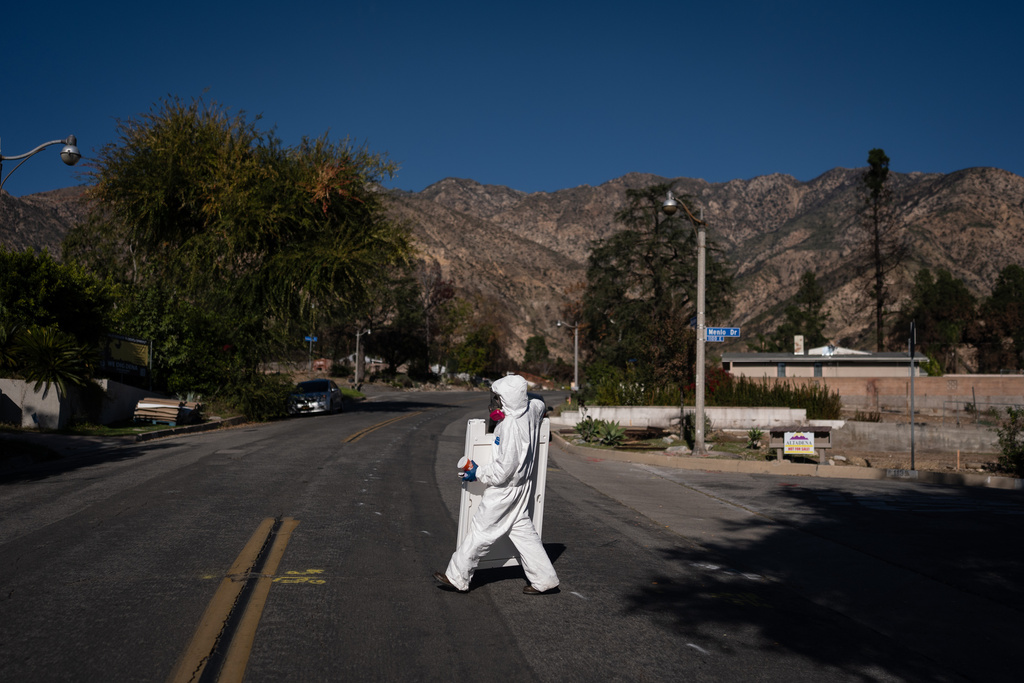 A worker in protective gear walks across a street while cleaning up a home that survived the Eaton Fire, Wednesday, Dec. 3, 2025, in Altadena, Calif. (AP Photo/Jae C. Hong)