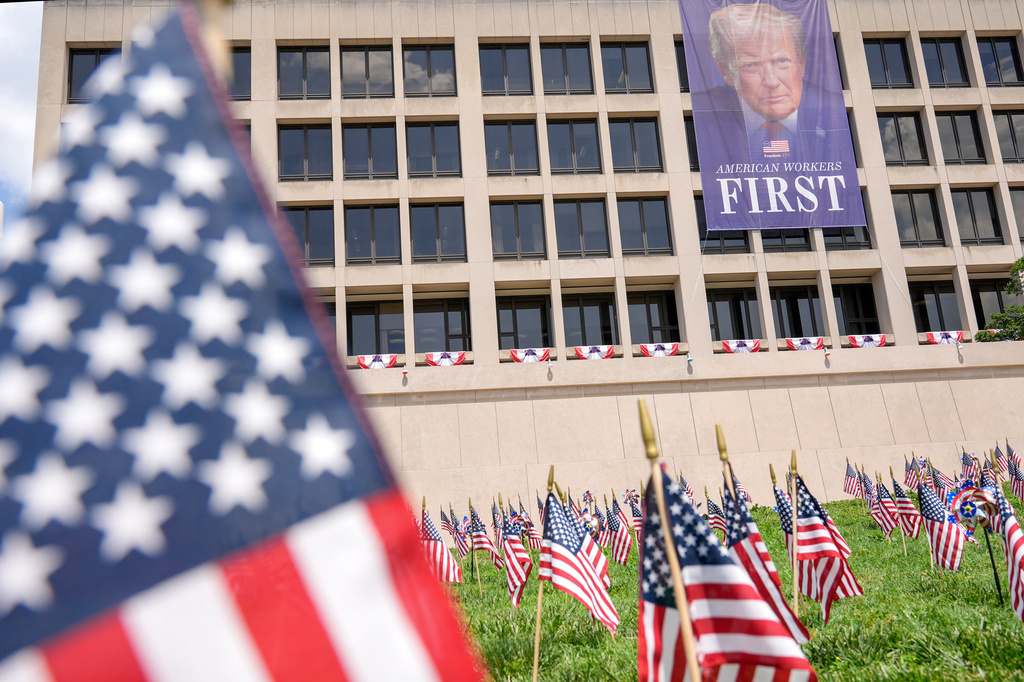 Flags are pictured in grass near a banner depicting a portrait of President Donald Trump, Thursday, July 2, 2026, on Capitol Hill in Washington. (AP Photo/Mariam Zuhaib)