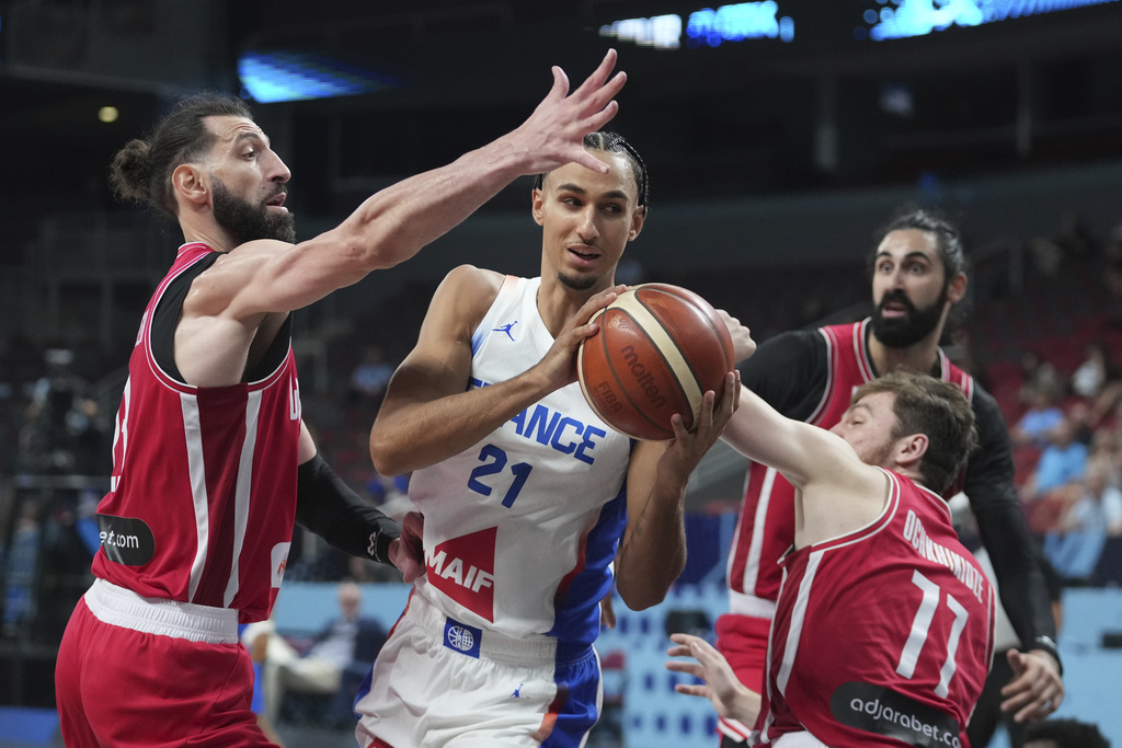 France's Zaccharie Risacher, centre, drives between Georgia's Tornike Shengelia, left, and Georgia's Giorgi Ochkhikidze during the Eurobasket, European Basketball Championship round of 16 match between France and Georgia at the Riga Arena in Riga, Latvia, Sunday, Sept. 7, 2025. (AP Photo/Sergei Grits)