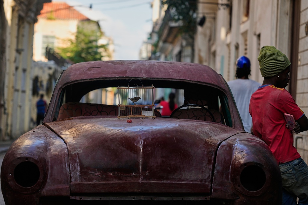 A bird in a cage sits for sale on the hood of a classic American car in Havana, Tuesday, Jan. 13, 2026. (AP Photo/Ramon Espinosa)