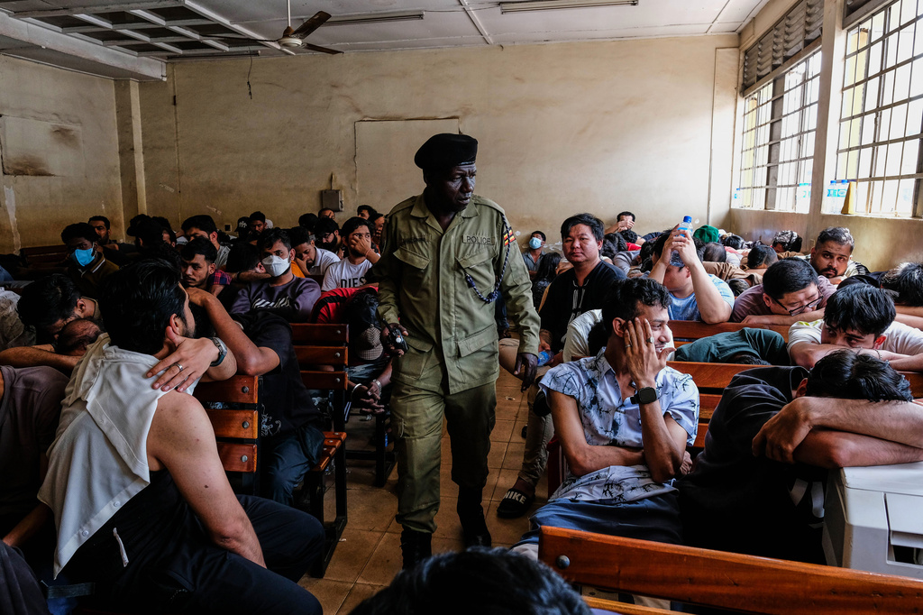 A Ugandan police officer walks past detainees seated in a room after authorities arrested dozens of foreigners in a crackdown on illegal migration, in Kampala, Uganda, Tuesday, April 28, 2026. (AP Photo/Hajarah Nalwadda)