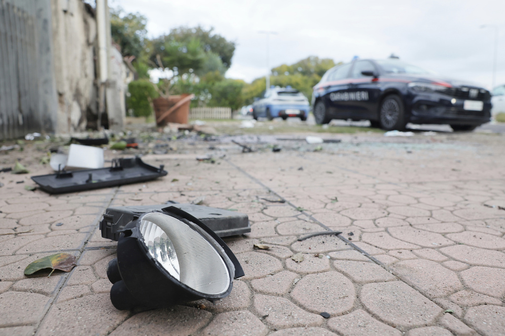 Parts of a car are seen on the ground as a Carabinieri military police car is parked outside the home of investigative journalist Sigfrido Ranucci after an explosive device detonated under the car, in Pomezia, Italy, Friday, Oct. 17, 2025. (Cecilia Fabiano/LaPresse via AP)