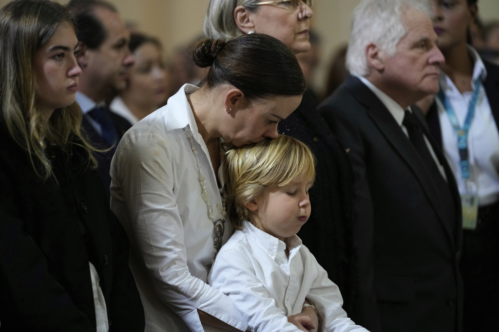 CORRECTS SPELLING OF TARAZONA'S MIDDLE NAME - Maria Claudia Tarazona kisses her son Alejandro during the funeral service for her husband, presidential hopeful and opposition Sen. Miguel Uribe, who died from wounds suffered when he was shot at a political rally, in Bogota, Colombia, Wednesday, Aug. 13, 2025. At right is Miguel Uribe, the senator's father. (AP Photo/Fernando Vergara)