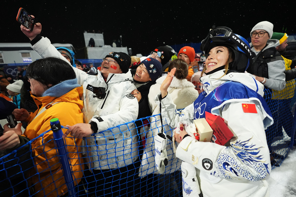 China's Eileen Gu takes photos with attendees after the women's freestyle skiing halfpipe qualifications at the 2026 Winter Olympics, in Livigno, Italy, Thursday, Feb. 19, 2026. (AP Photo/Lindsey Wasson)