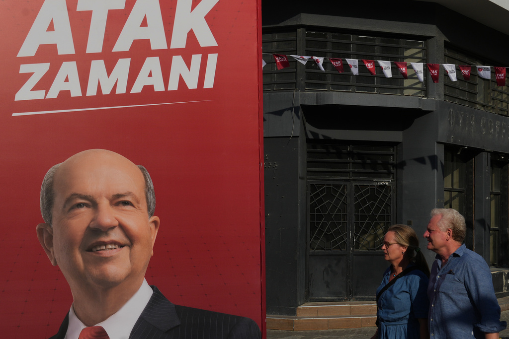 A couple walk past a campaign poster of Turkish Cypriot leader and candidate Ersin Tatar ahead of the Turkish Cypriot elections in the Turkish occupied northern part of divided Nicosia, Cyprus, Friday, Oct. 17, 2025. (AP Photo/Petros Karadjias)