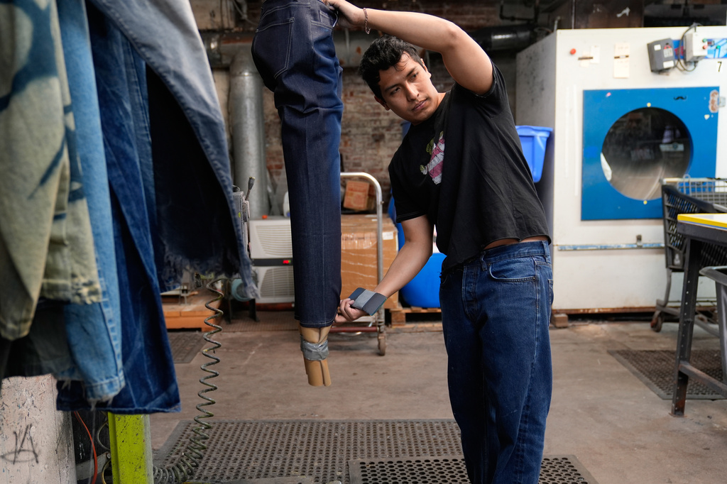 Bryan Morales Ibarra distresses denim by hand at the BPD Washhouse, a denim processing facility, in Jersey City, N.J., Tuesday, May 5, 2026. Behind him is a machine that uses ozone as part of the distressing process, as opposed to the traditional washing and chemicals. (AP Photo/Seth Wenig)
