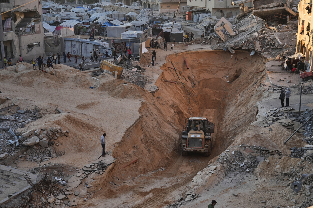 Palestinians watch members of the Hamas militant group searching for bodies of the hostages in Khan Younis, southern Gaza Strip, Saturday, Oct. 18, 2025. (AP Photo/Jehad Alshrafi)