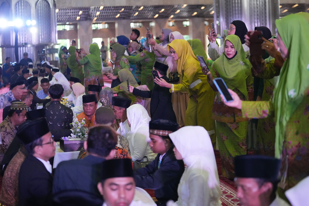 Family members use their phones to take photos during a mass wedding ceremony at Istiqlal Mosque in Jakarta, Indonesia, Wednesday, Dec. 3, 2025. (AP Photo/Tatan Syuflana)