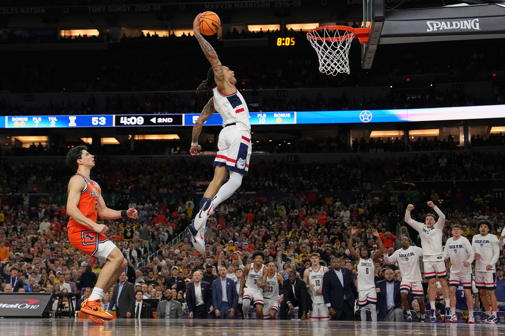 UConn's Solo Ball (1) dunks as Illinois' Andrej Stojakovic, left, watches during the second half of an NCAA college basketball tournament semifinal game at the Final Four, Saturday, April 4, 2026, in Indianapolis. (AP Photo/Michael Conroy)