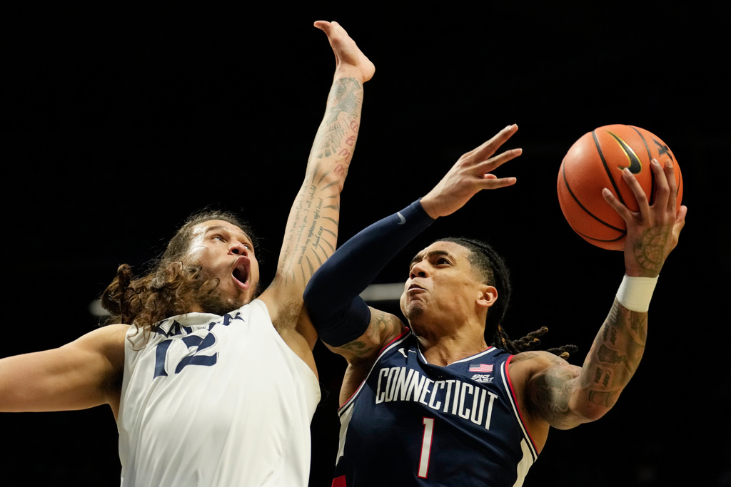 UConn guard Solo Ball (1) drives to the basket as Xavier forward Tre Carroll (12) defends during the second half of an NCAA college basketball game, Wednesday, Dec. 31, 2025, in Cincinnati. (AP Photo/Carolyn Kaster)