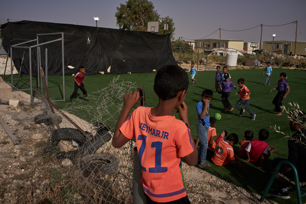 Boys and girls play on a small soccer pitch, with caravans from the nearby Israeli settlement of Carmel visible in the background, in the West Bank Bedouin village of Umm al-Khair, Tuesday, May 12, 2026. (AP Photo/Leo Correa)