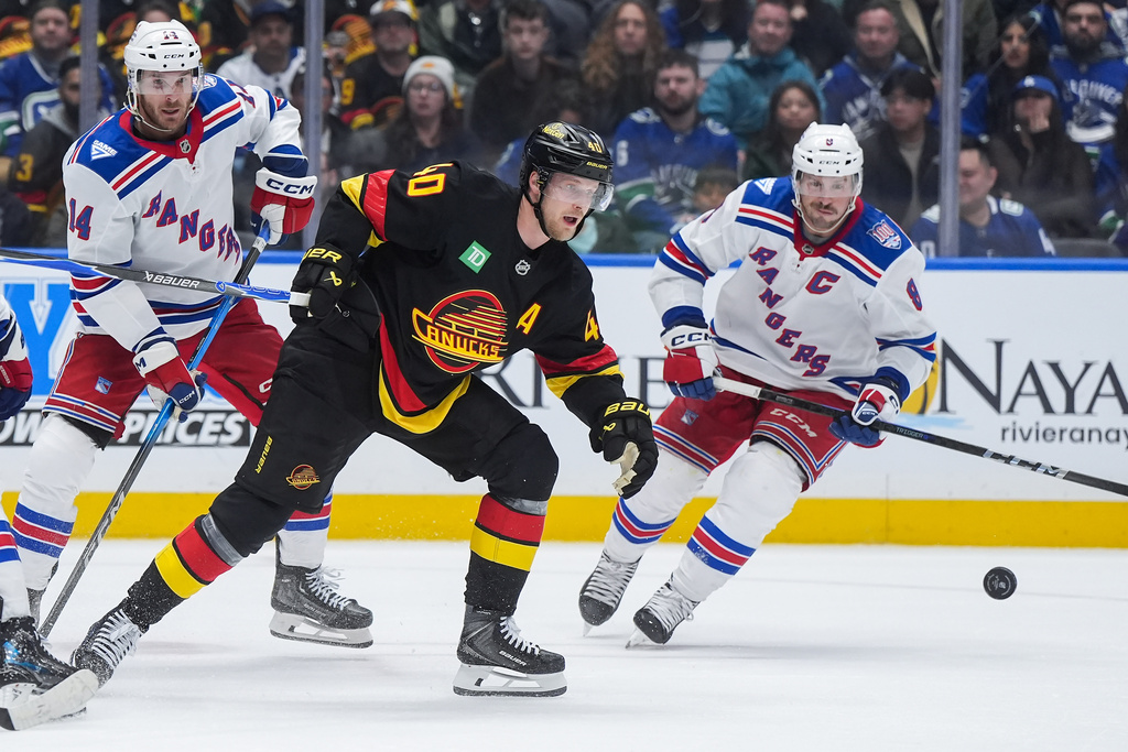 Vancouver Canucks' Elias Pettersson (40) and New York Rangers' J.T. Miller (8) skate after the puck as Taylor Raddysh (14) watches during the third period of an NHL hockey game in Vancouver, on Tuesday, Oct. 28, 2025. (Darryl Dyck/The Canadian Press via AP)